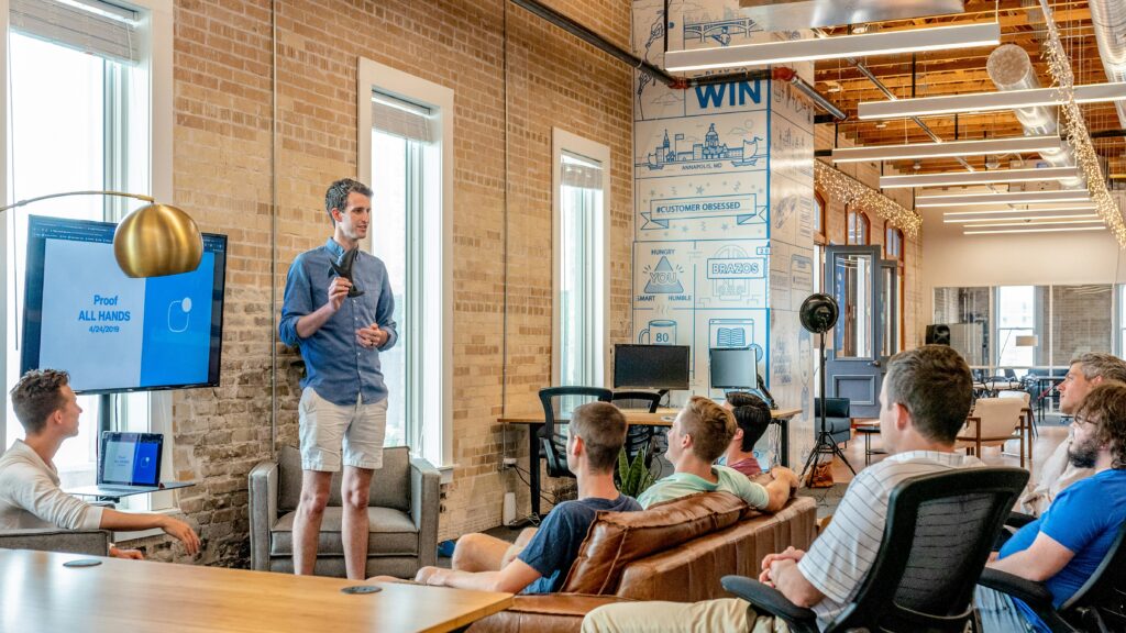 Young man presenting a prototype to his team members in front of a big office area.