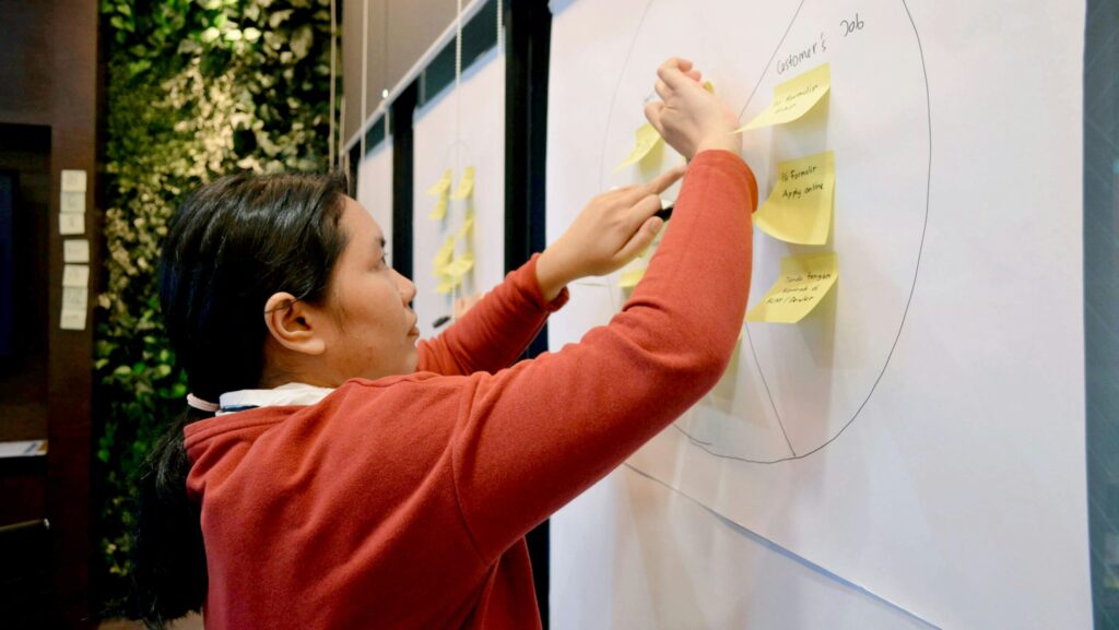 Woman placing sticky nodes on a value proposition canvas on a white board.